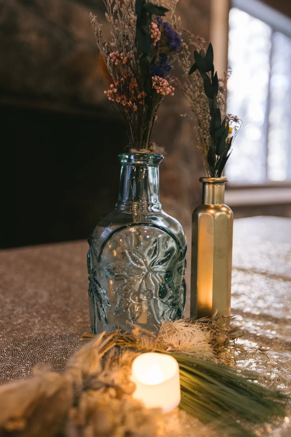Table detail with vintage glass bottles, dried stems and candlelight