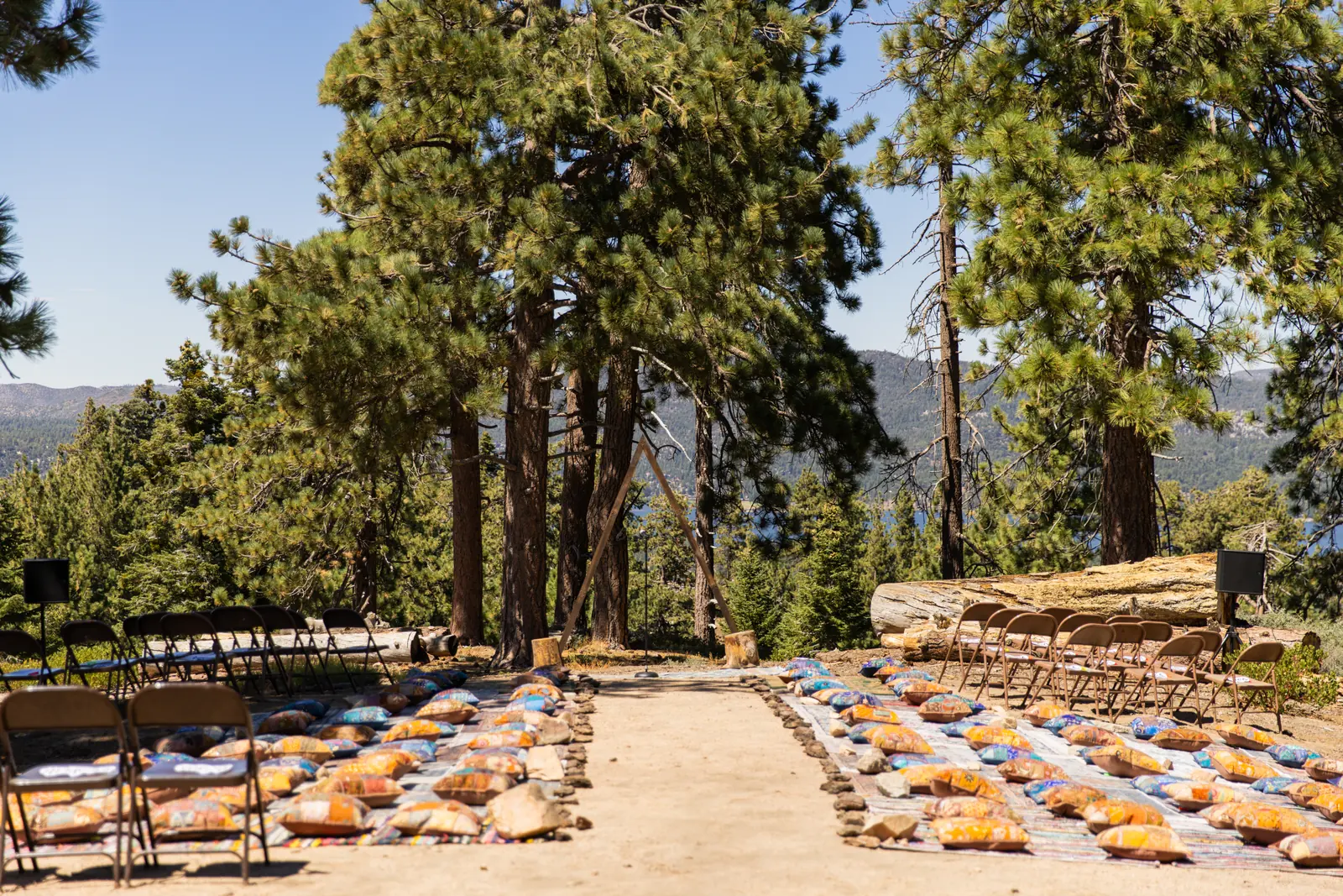 Boho ceremony aisle lined with floor cushions and rugs among mountain pines